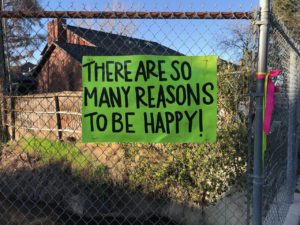 sign attached to a chainlink fence that says, "There are so many reasons to be happy!"