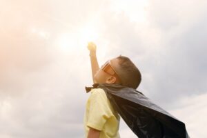Kid with superhero cape punching the sunshine