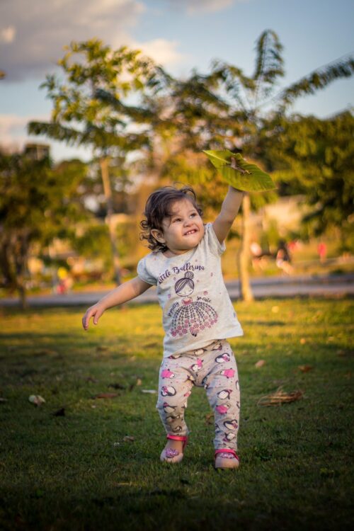 toddler with leaf playing on a grassy lawn