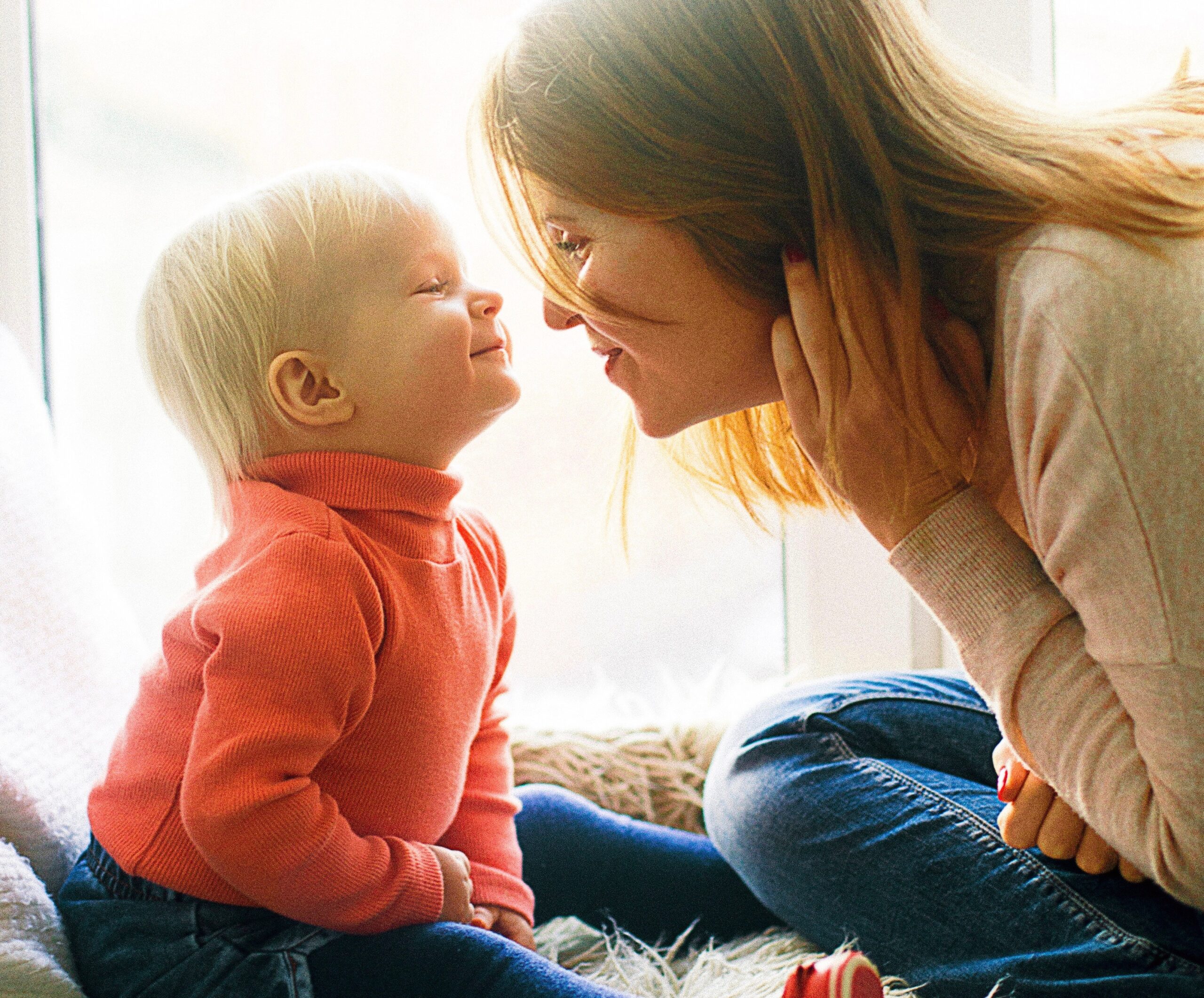 woman and child sitting on fur covered bed in front of window nose to nose with smiles