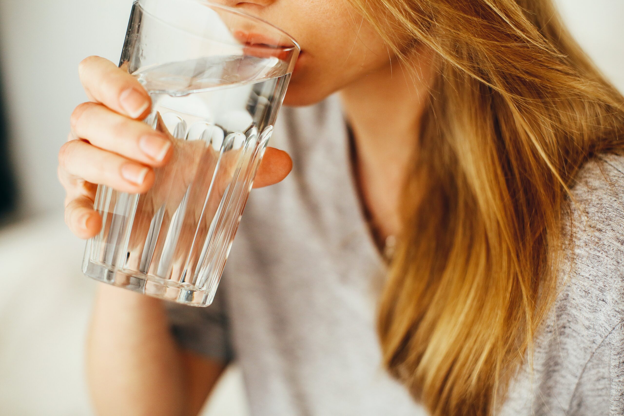 woman drinking a glass of water with a v-neck light gray t-shirt on.