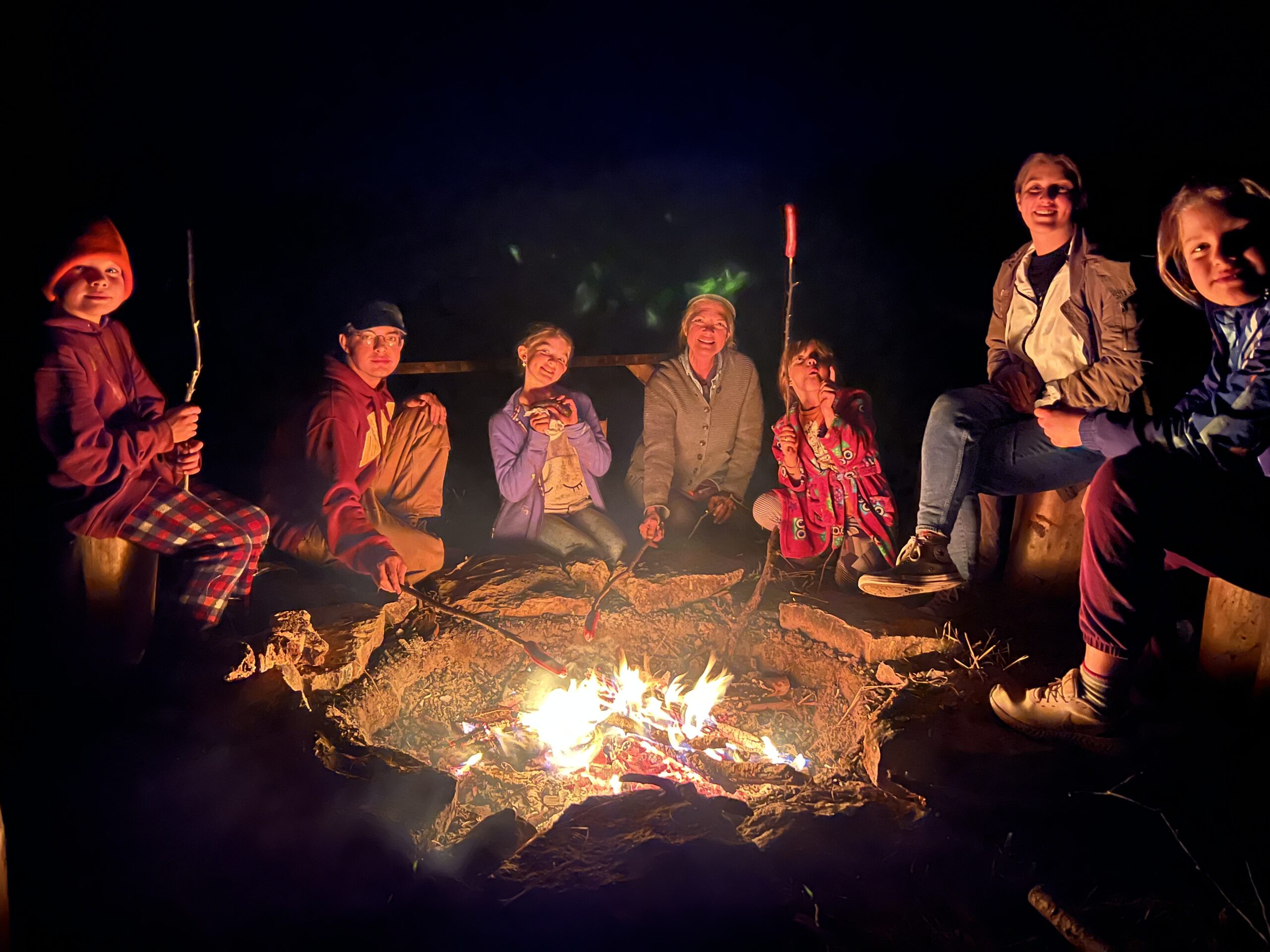 family roasting hotdogs around a camp fire